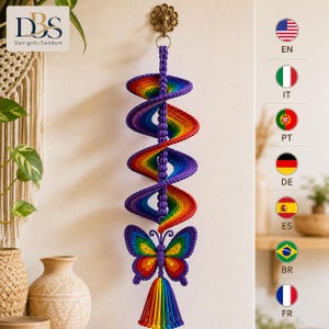 May include: A hanging spiral decoration crafted from purple yarn with a rainbow-colored inner edge. The structure features a central column of knotted purple cord, ending in a butterfly ornament with rainbow wings and a multi-colored yarn tassel.