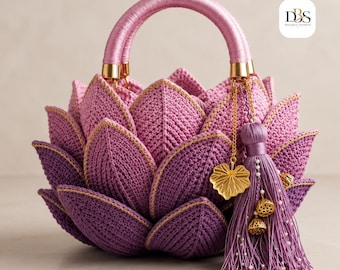 Puede incluir: Un bolso de ganchillo con forma de flor de loto en tonos morados y rosas. El bolso presenta pétalos en capas, un asa envuelta y una borla decorativa con dijes dorados en forma de hoja y vaina de loto. El logotipo DBS Design-Season es visible.