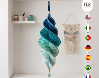 May include: A hanging spiral decoration made of crocheted yarn in an ombre gradient of blue, teal, and light green. The piece features a wooden bead at the top and bottom, with a small green glass pendant attached to the lowest bead for display.