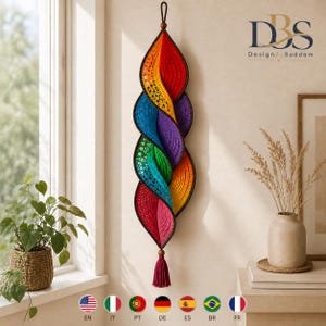 May include: A vertical hanging wall decoration featuring a spiral design made of crocheted fabric in a rainbow gradient of red, orange, yellow, green, blue, and purple. The piece has a dark brown border, a top hanging loop, and a bottom tassel.