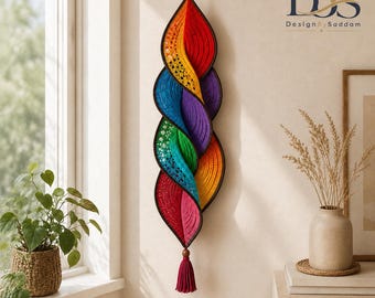 Könnte beinhalten: Eine vertikale Wanddekoration mit einem Spiraldesign aus gehäkeltem Stoff in einem Regenbogenverlauf aus Rot, Orange, Gelb, Grün, Blau und Violett. Das Stück hat einen dunkelbraunen Rand, eine Aufhängeschlaufe oben und eine Quaste am unteren Ende.