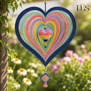 Puede incluir: Un móvil de ganchillo en forma de corazón con marcos concéntricos en azul oscuro, verde menta, rosa y amarillo. Un pequeño corazón relleno multicolor cuelga en el centro, adornado con cuentas y un dije cuadrado de ganchillo con una borla.