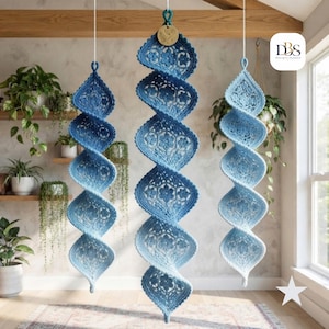 Peut inclure: Trois décorations suspendues en spirale réalisées en dentelle au crochet bleue et blanche. Chaque pièce présente un motif floral répétitif et une forme torsadée effilée. L'ornement central comporte une petite étiquette en bois avec un motif de feuille.