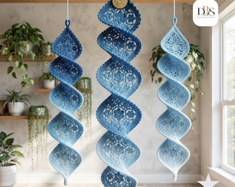 May include: Three hanging spiral ornaments crafted from blue and white crochet lace. Each piece features a repeating floral pattern and a tapered, twisted shape. The center ornament includes a small wooden tag with a leaf design at the top.