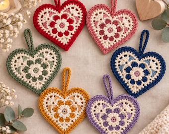 Puede incluir: Seis adornos de ganchillo en forma de corazón con un motivo floral central en rojo, rosa, verde, amarillo, azul y morado, cada uno con un borde de encaje color crema y un lazo de hilo a juego para colgar, dispuestos en círculo.