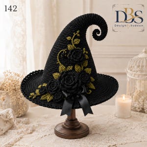 May include: A black crocheted witch hat with a curled tip, adorned with dark crocheted roses and olive green crocheted leaves. A black satin ribbon bow is attached to the base. The number 142 and the text DesignBySaddam are visible.
