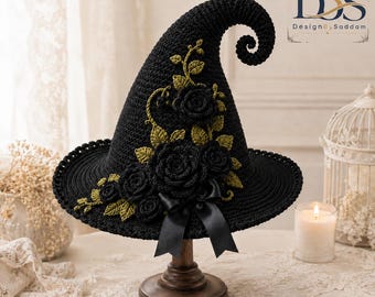 Puede incluir: Un sombrero de bruja de ganchillo negro con punta curvada, adornado con rosas de ganchillo oscuras y hojas de ganchillo verde oliva. Un lazo de cinta de satén negro está sujeto a la base. El número 142 y el texto DesignBySaddam son visibles.