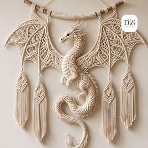 May include: A cream-colored macrame wall hanging featuring a detailed dragon with intricate knotted wings and a long, curved tail. The dragon is suspended from a horizontal wooden branch and includes four decorative tassels hanging from the wings.