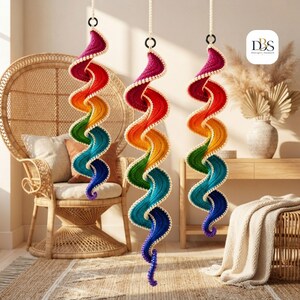 May include: Three hanging spiral decorations featuring a vibrant rainbow gradient of crocheted yarn. Each spiral transitions from deep magenta at the top through orange, yellow, green, and blue, ending in violet, with a white crocheted edge.