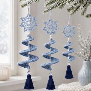 Könnte beinhalten: Drei hängende Ornamente mit einem hellblauen Häkelstern an der Spitze, einem spiralförmigen hellblauen Häkelkörper und einer dunkelblauen Quaste am unteren Ende. Jedes Ornament ist mit kleinen weißen Perlen und einer Kristallperle verziert.