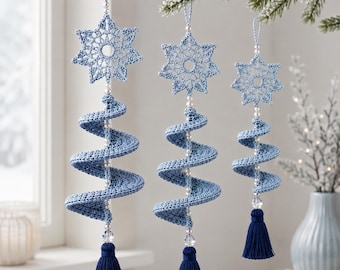 Puede incluir: Tres adornos colgantes con una estrella de ganchillo azul claro en la parte superior, un cuerpo en espiral de ganchillo azul claro y una borla azul oscuro en la parte inferior. Cada adorno tiene pequeñas cuentas blancas y una cuenta de cristal.