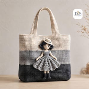 May include: A crochet tote bag featuring a color-blocked design in cream, light gray, and dark gray. Attached to the front is a three-dimensional crochet doll figure wearing a gray dress, a matching hat, and dark boots. The logo DBS is visible.