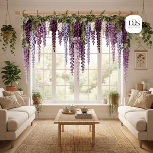 Può includere: Una decorazione da parete con fiori artificiali di glicine a cascata in tonalità viola, lavanda e bianco, appesi a un bastone di legno orizzontale. La composizione floreale include foglie verdi ed è esposta sopra una finestra.