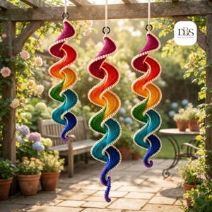 May include: Three hanging spiral decorations made of crocheted yarn in a vibrant rainbow gradient of red, orange, yellow, green, blue, and purple. Each spiral features a white crocheted edge and is suspended by a white cord from a black ring.
