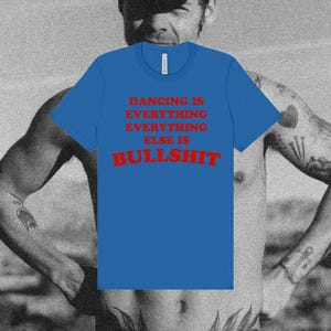 Könnte beinhalten: Ein leuchtend blaues T-Shirt mit kurzen Ärmeln und rotem Text auf der Vorderseite, der lautet: DANCING IS EVERYTHING EVERYTHING ELSE IS BULLSHIT. Das Kleidungsstück hat einen Rundhalsausschnitt und eine Standardpassform in klarer Ansicht.