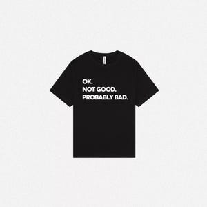 Pode incluir: Uma t-shirt preta de manga curta com texto branco impresso no peito que diz: OK. NOT GOOD. PROBABLY BAD. A pe&ccedil;a tem um decote redondo padr&atilde;o e uma bainha reta, apresentada num estilo plano para uma visibilidade clara do design.