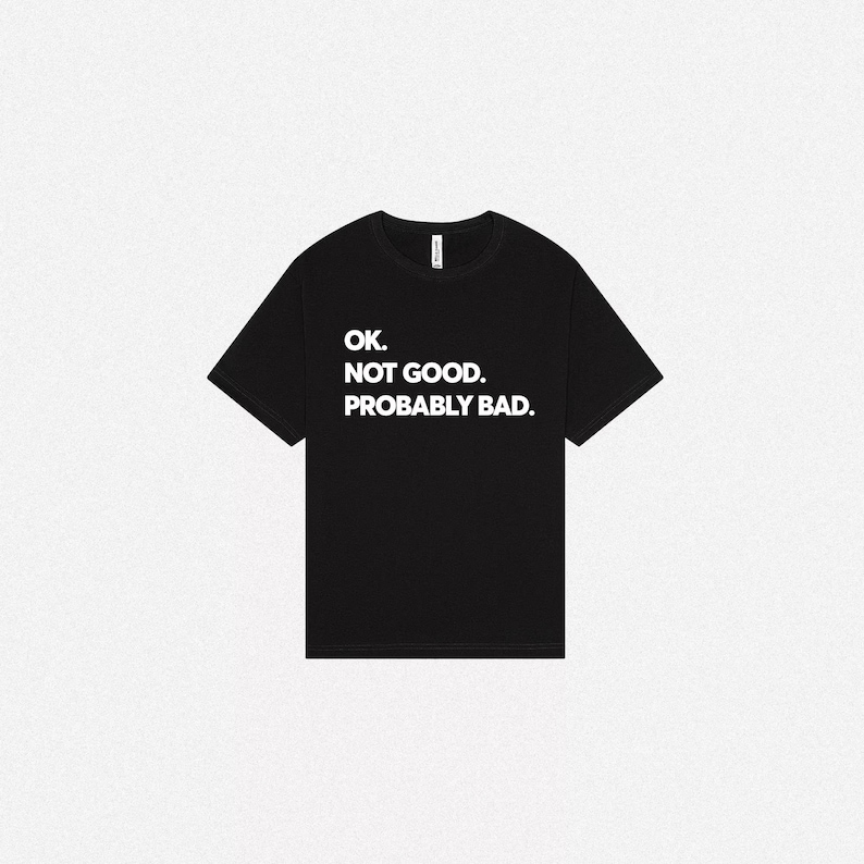 Pode incluir: Uma t-shirt preta de manga curta com texto branco impresso no peito que diz: OK. NOT GOOD. PROBABLY BAD. A pe&ccedil;a tem um decote redondo padr&atilde;o e uma bainha reta, apresentada num estilo plano para uma visibilidade clara do design.