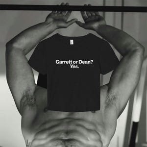 May include: A black short-sleeved crew neck t-shirt featuring the white printed text "Garrett or Dean? Yes." centered on the chest. The garment has a standard fit with a round neckline and short sleeves, presented in a clear, straightforward design.