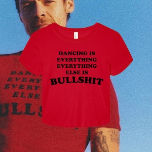 Könnte beinhalten: Ein leuchtend rotes Kurzarm-T-Shirt mit schwarzem Text, der DANCING IS EVERYTHING EVERYTHING ELSE IS BULLSHIT lautet. Das Shirt hat einen Rundhalsausschnitt und eine bauchfreie Passform, wobei die Botschaft deutlich auf der Brust zu sehen ist.