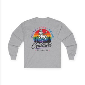 May include: A heather gray long-sleeve shirt featuring a graphic of a centaur holding a hockey stick. The design includes a rainbow-colored sun, a city skyline silhouette, and the text PEACE LOVE PRIDE Centaurs OTTAWA, ON.