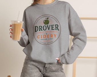 May include: A heather gray long-sleeve crewneck sweatshirt featuring a circular graphic on the chest. The design includes a green apple icon and the text: FOURTH GENERATION ORCHARDS, DROVER FAMILY ORCHARDS & CIDERY, DROVER CIDER, EST 2010, OTTAWA.