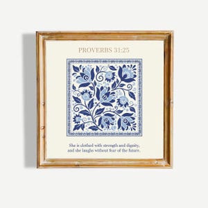 Peut inclure: Une décoration murale carrée encadrée avec un fond crème et un motif floral bleu au centre. Le texte indique PROVERBS 31:25 en haut et She is clothed with strength and dignity, and she laughs without fear of the future en bas.