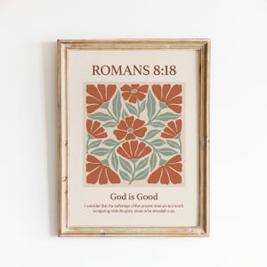 Könnte beinhalten: Ein gerahmter Wandkunstdruck mit dem Text ROMANS 8:18 oben, einem zentralen Blumenmuster mit rostorangen Blüten und salbeigrünen Blättern auf cremefarbenem Grund sowie dem Text God is Good mit dem Vers darunter in brauner Schrift.