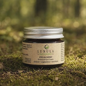 Könnte beinhalten: Ein kleines, dunkles Glastiegelchen mit Lunula Botanique Eye Alchemy botanischer Augencreme und einem silbernen Metallschraubdeckel. Das beigefarbene Etikett enthält schwarzen Text, den Markennamen, die Produktbezeichnung und ein Mondsichel-Logo.