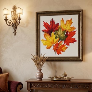May include: A square framed wall art piece featuring a vibrant illustration of autumn maple leaves in shades of red, orange, yellow, and green. The artwork is displayed in a dark brown ornate frame, centred on a light beige wall above a wooden console.