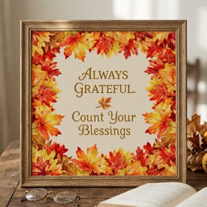 May include: A square framed cross-stitch embroidery featuring a border of vibrant red, orange, and yellow autumn maple leaves surrounding the text Always GRATEFUL. Count Your Blessings in brown lettering on a cream-coloured fabric background.