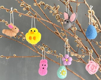 May include: A display of Easter-themed felt ornaments hanging from pussy willow branches. The ornaments include a brown bunny, yellow chick, gray bunny, blue egg, pink Peep, flower, decorated egg, and a pink rose.