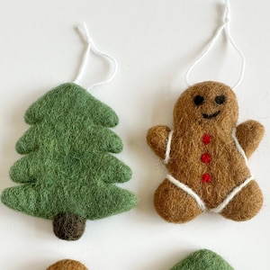 May include: Four felt Christmas ornaments, two green Christmas trees and two gingerbread men. The ornaments are brown, green, white and red.