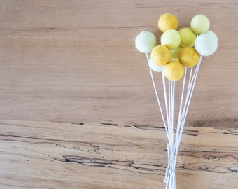 May include: A bunch of yellow and green felt balls on white stems. The balls are arranged in a cluster, with the stems extending downwards.