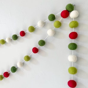 May include: A festive garland made of felt balls in red, green, and white. The garland is strung together with white thread and is perfect for decorating for the holidays.
