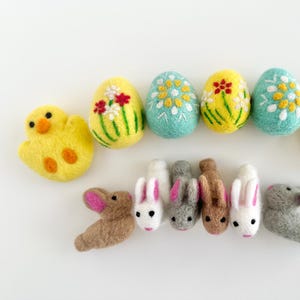 May include: A set of felt Easter decorations including six colorful eggs, two yellow chicks, and six bunnies in various colors. The eggs are decorated with flowers and leaves.