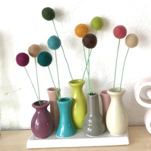 May include: A set of seven small ceramic vases in various colors, arranged on a white tray. The vases hold colorful felt ball stems, creating a whimsical and modern floral arrangement.