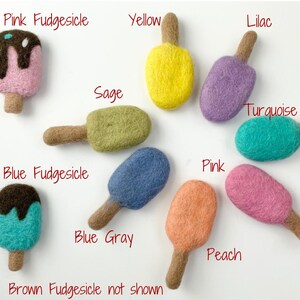 May include: A collection of colorful felt ice pops in various shades including pink, yellow, lilac, sage, turquoise, blue, and peach. Each ice pop has a brown stick. Text labels identify each color, including "Pink Fudgesicle" and "Blue Fudgesicle."