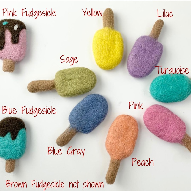 May include: A collection of colorful felt ice pops in various shades including pink, yellow, lilac, sage, turquoise, blue, and peach. Each ice pop has a brown stick. Text labels identify each color, including "Pink Fudgesicle" and "Blue Fudgesicle."