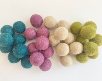 May include: A collection of felt balls in various colors, including teal, purple, beige, and green. The balls are arranged in three groups, with the teal balls on the left, the purple balls in the center, and the beige and green balls on the right.
