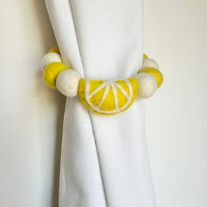 May include: Yellow and white felt ball curtain tieback with a lemon slice design.