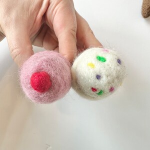 Pode incluir: Duas bolas de feltro, uma rosa com um centro vermelho e uma branca com confeitos coloridos.