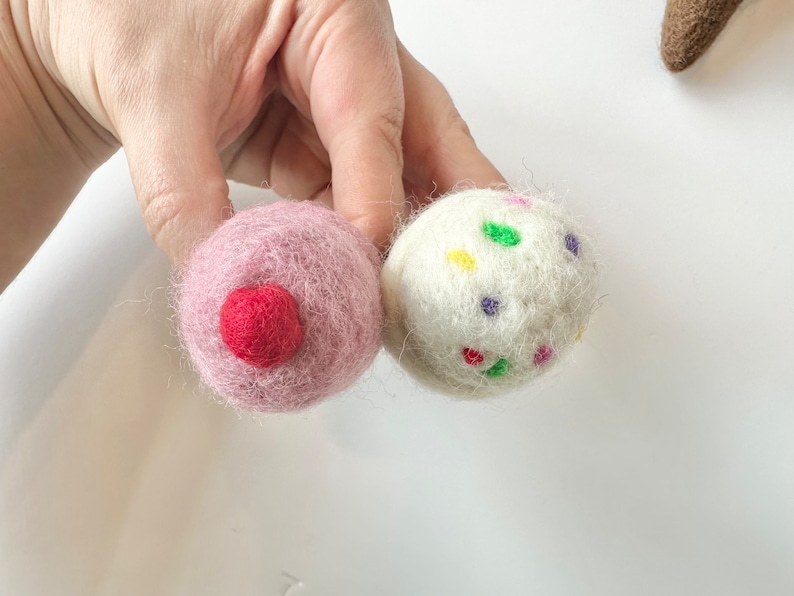 Pode incluir: Duas bolas de feltro, uma rosa com um centro vermelho e uma branca com confeitos coloridos.