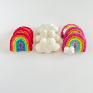 May include: Three felt rainbow arches and two felt clouds. The rainbows are layered with red, orange, yellow, green, blue, indigo, and violet. The clouds are white.