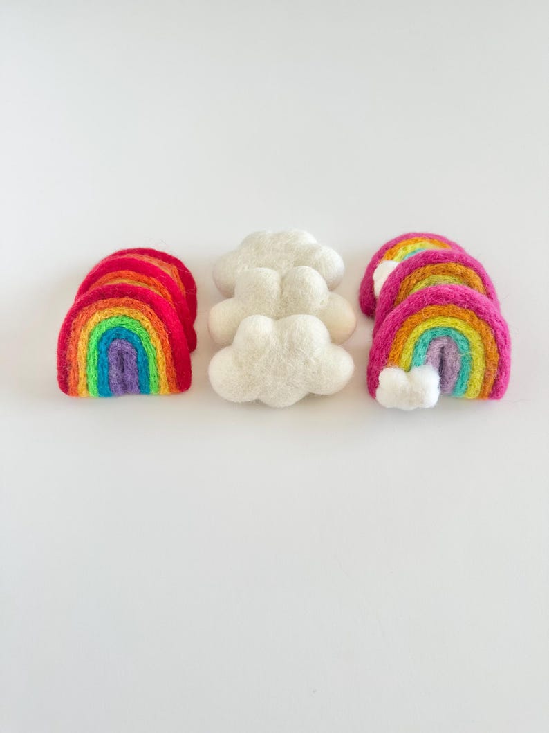 May include: Three felt rainbow arches and two felt clouds. The rainbows are layered with red, orange, yellow, green, blue, indigo, and violet. The clouds are white.