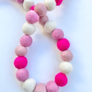 May include: A garland of pink, white, and hot pink felt balls. The balls are strung together on a white string.