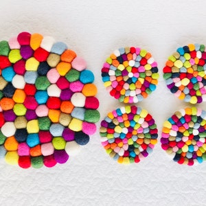 May include: Set of five colorful felt coasters, each made of a spiral of small, round balls in various shades of pink, blue, green, yellow, orange, red, and white. The largest coaster is about 12 inches in diameter.