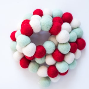 May include: A garland of red, white, and green felt balls. The balls are arranged in a circular pattern and are strung together with a white thread.