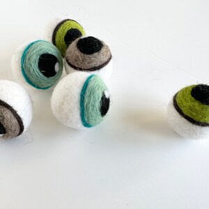 May include: Five white felt balls with different colored eyes. The eyes are green, brown, and blue. The balls are all about the same size and are arranged in a cluster.