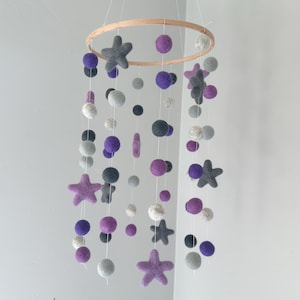 May include: A purple and gray felt baby mobile with stars and balls hanging from a wooden ring.