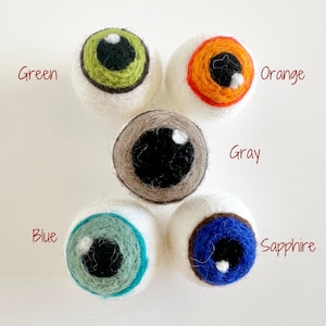 May include: Five felt wool eyeballs with different colored irises. The colors are green, orange, gray, blue, and sapphire.